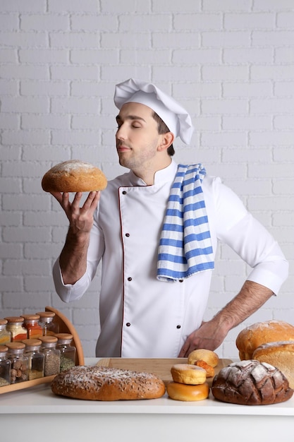 Baker in kitchen at table with freshly loaves of bread on white brick wall background