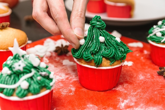 Пекарь делает рождественское угощение Рождественская елка в форме кексов Руки выжимают вкусный крем из пакета для глазури поверх праздничных тортов Глазурь и украшение помадными тортами и кексами