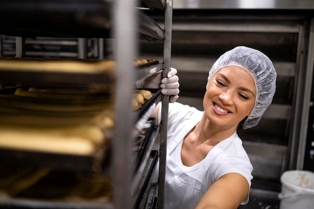 Baker moving trays with bread or dough to the oven for baking process