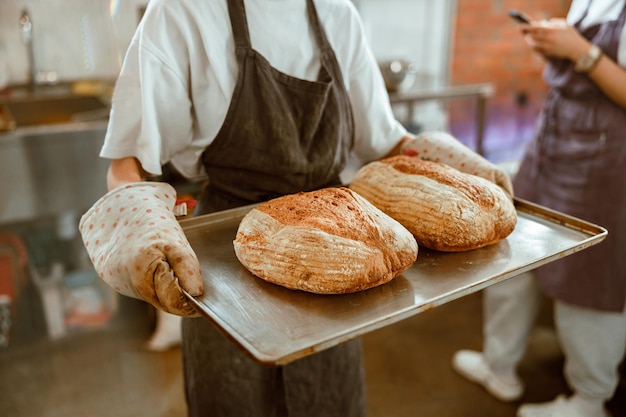 Baker in oven mitts holds large tray with breads in craft workshop