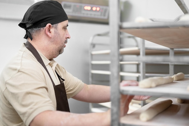 Foto panettiere che posiziona il vassoio con la pasta cruda formata su un carrello a cremagliera pronto per la cottura in forno foto di alta qualità