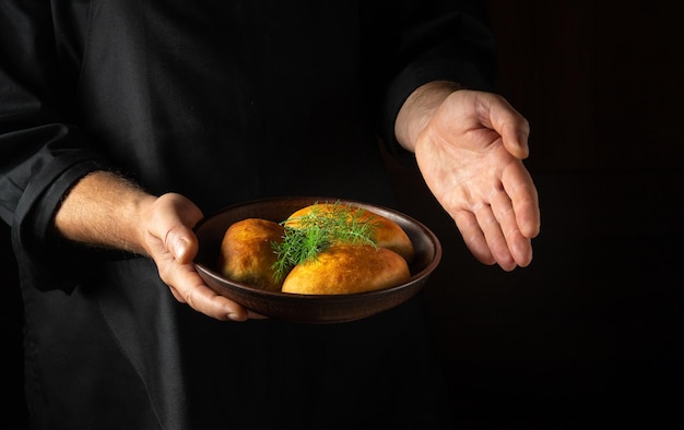 The baker presents in his hand a plate of freshly baked buns or dill pies Free black space for menu or recipe