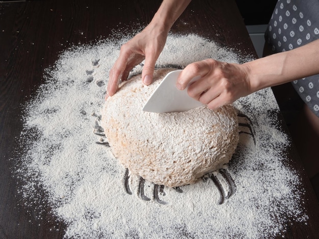 La mano del panettiere taglia la pasta cruda senza lievito su uno sfondo scuro con un coltello di plastica