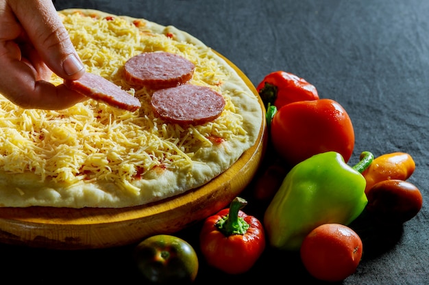 La mano del panettiere che mette gli ingredienti sulla salsiccia per pizza