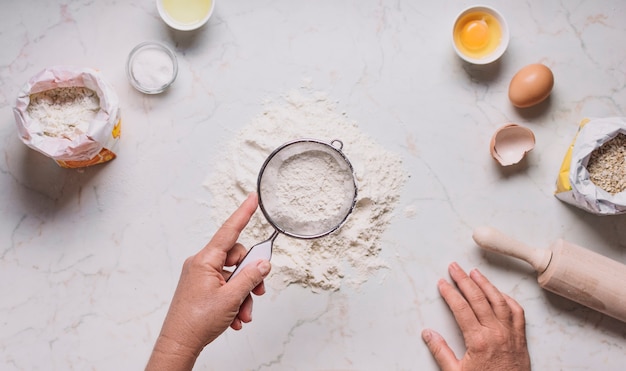 Photo baker's hand sifting flour by sieve on kitchen counter