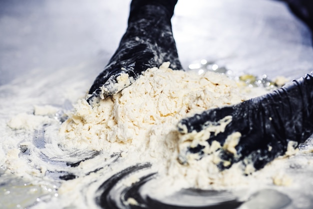 Baker's hands in black gloves knead the dough.