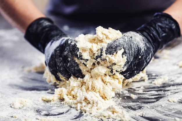 Baker's hands in black gloves knead the dough.