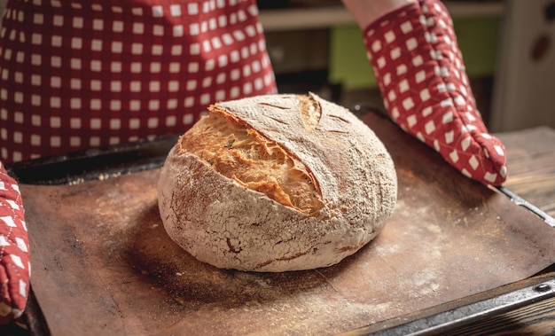 Le mani del fornaio che tengono pane naturale fatto in casa con una crosta dorata su un tovagliolo su fondo di legno vecchio stile rustico