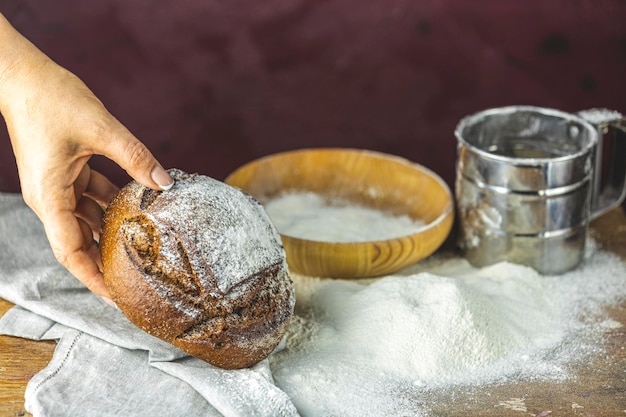写真 パンを持つパン屋の手ハイコントラストの写真小麦粉と暗い木のテーブルにライ麦パンを持つ女性の手