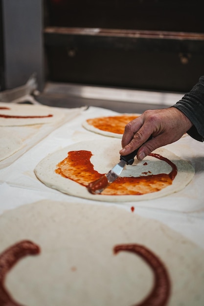 Baker smeert tomatensaus op het pizzadeeg voordat het wordt gebakken