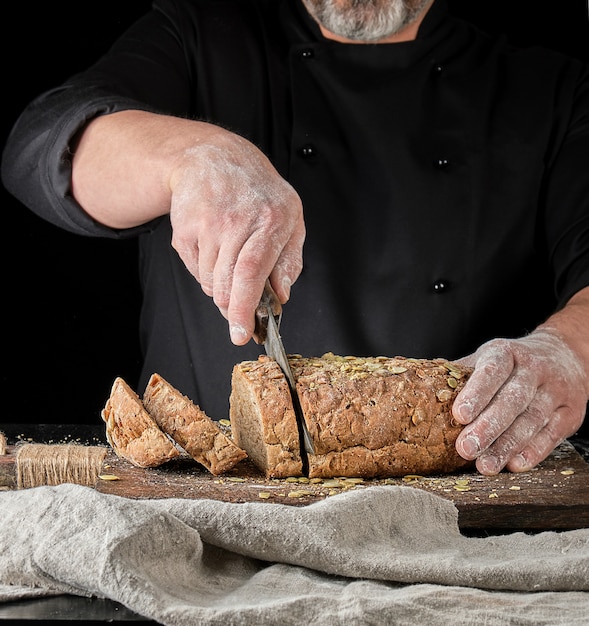 Baker snijdt een mes in sneetjes roggebrood met pompoenpitten