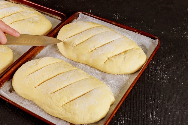 Baker snijdt ongekookt brooddeeg op rek klaar om te bakken