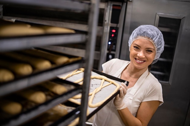 baker in white uniform and hairnet working in bakery production moving tray with raw bread