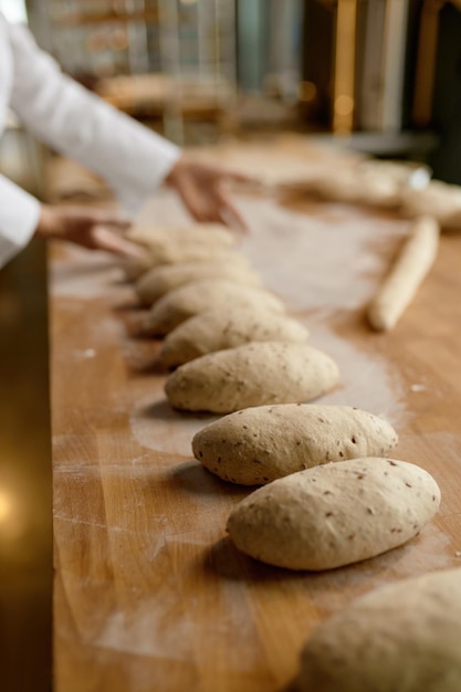 Baker working in bakery, forming baguettes from raw dough. Bakery shop and manufactory concept