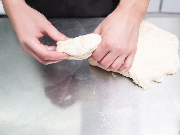 Baker works with dough on a metal work surface. Professional cook making rolls or buns