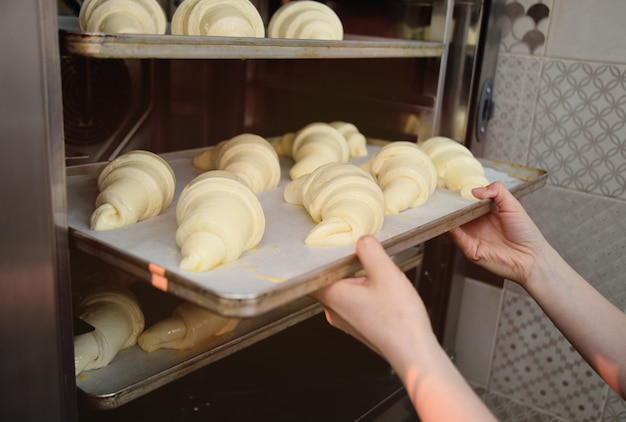 Baker zet rauwe croissants van de bakkerij in de oven