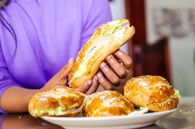 Photo bakers hand showing a sandwich with open bread with cheese ham lettuce and mayonnaise on a plate on a table for breakfast