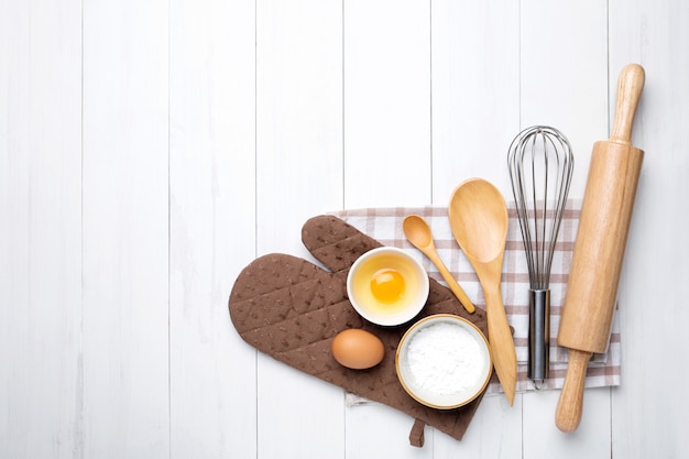 Photo bakery ingredients. wheat ears and bowl of flour, egg, rolling pin, egg whisk on white