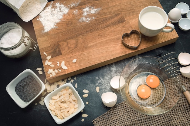 Bakery process. Healthy baking ingredients - flour, almond nuts, eggs, milk on the black background. Top view, flat lay. Modern cooking composition. Kitchen utensils.