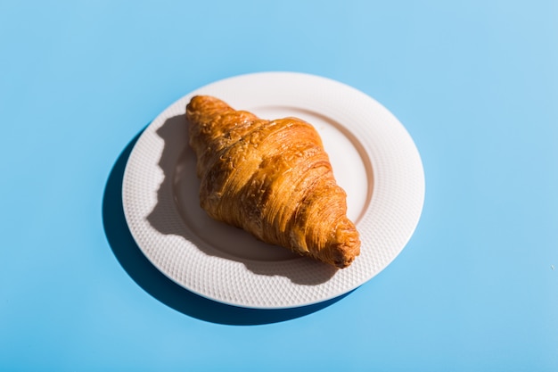 Bakery products baked croissant on white plate. Blue background, top view close-up. Pop art style. Summer shadows. Delicious and food concept.