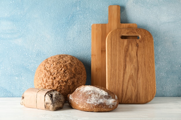 Bakery products and cutting boards on white wooden table against light space, space for text