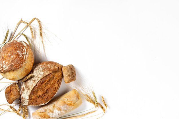 Bakery. Set of freshly baked crispy bread and buns with ears of wheat on white background with copy space, top view flat lay