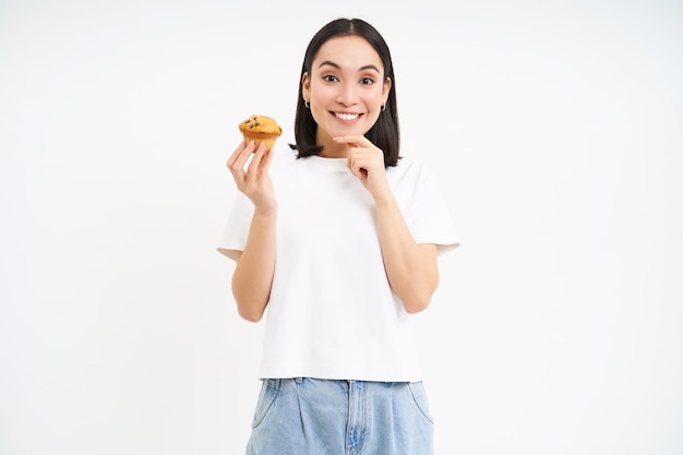 Bakery and sweets happy asian woman looking at tasty cupcake eating pastry white background