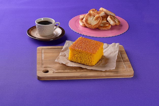 Bakery sweets on a wooden board with a carrot cake and French bread in the background beside a cup o