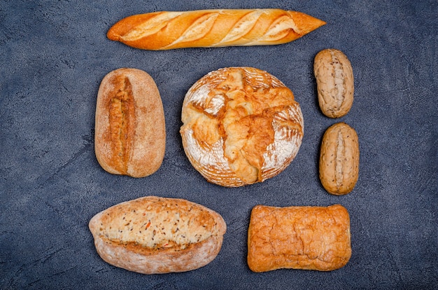 Bakery - various rustic crispy buns with bread and rolls on a dark background.