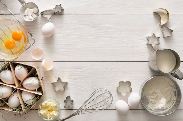 Baking background. Cooking ingredients for dough and pastry, eggs, flour and cookie cutter on white rustic wood. top view