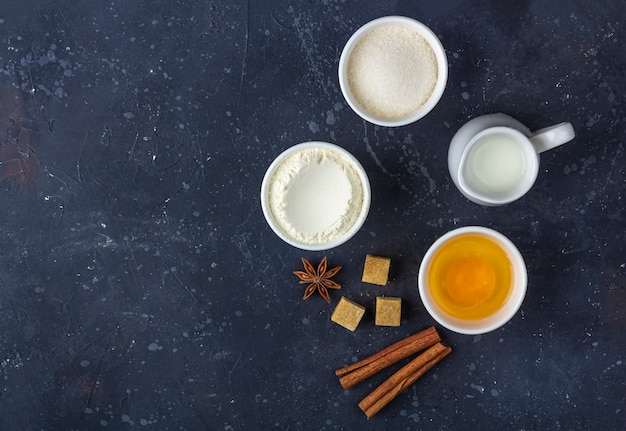 Baking background. Ingredients for cooking cake in bowls on dark table. Food concept.