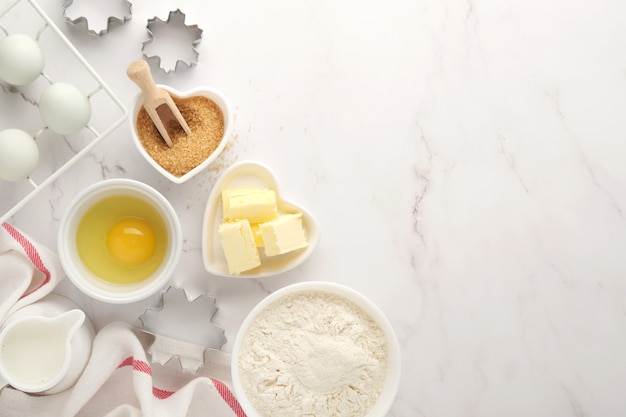 Baking background with flour, eggs, kitchen tools, utensils and cookie molds on white marble table. Top view. Flat lay style. Mock up.