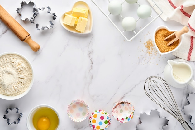 фон выпечки с мукой, яйцами, кухонными принадлежностями, посудой и формами для печенья на белом столе