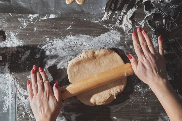 Biscotti di natale di cottura sulla tavola di legno marrone scuro. famiglia che fa l'uomo di pan di zenzero, tagliando i biscotti di pasta di pan di zenzero, vista dall'alto