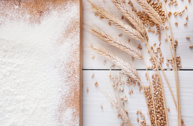 Baking class or recipe concept, sprinkled wheat flour, grain and ears. Top view on wooden board on table. Cooking dough or pastry.