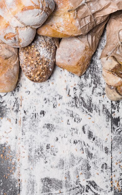 Baking and cooking concept background. Border of different bread sorts, wrapped in craft paper top view with copy space on wooden table, sprinkled with flour, vertical