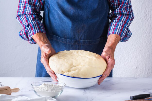 집에서 빵 굽기 건강한 음식과 생활 방식 개념 부엌 식탁에 있는 파이에 필링을 퍼뜨리는 핀으로 손으로 신선한 반죽을 반죽하는 수석 제빵사