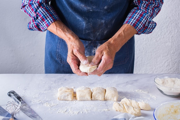 Baking eating at home healthy food and lifestyle concept Senior baker man cooking kneading fresh dough with hands rolling with pin spreading the filling on the pie on a kitchen table with flour