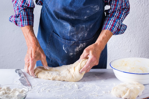 Baking eating at home healthy food and lifestyle concept Senior baker man cooking kneading fresh dough with hands rolling with pin spreading the filling on the pie on a kitchen table with flour