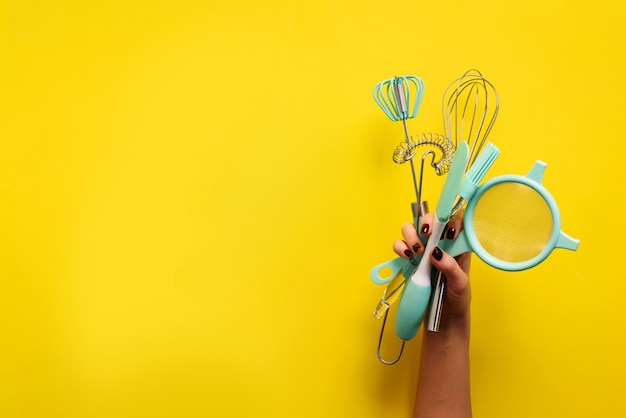 Baking flat lay. Female hands holding kitchen tools, sieve, rolling pin, spatula and bruch on yellow background. Banner with copy space