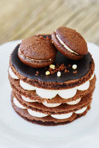 Baking homemade chocolate cake with biscuit, meringue and macaroons in white plate on wooden table. Festive sweet dessert birthday decoration macarons