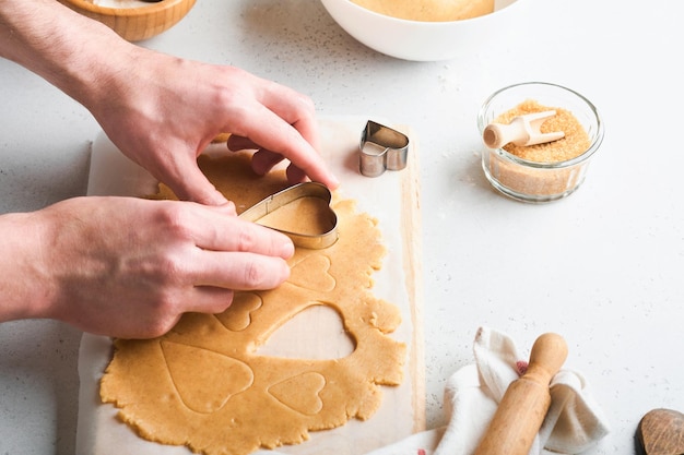 白い背景の上のベーキング材料と台所用品上面図ハートシュガークッキーを準備する女性または男性の手シュガークッキーを焼く台所のテーブルに小麦粉の卵シュガースパイスフラットレイ