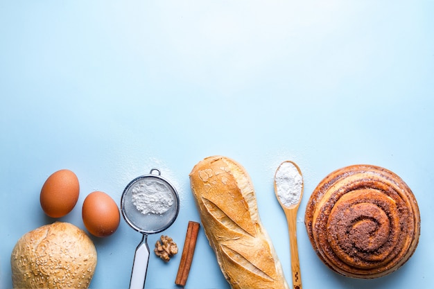 Baking ingredients for bakery products. Fresh crisp bread, baguette and buns on a blue background.