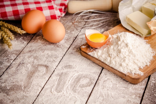Ингредиенты для выпечки мука яйца масло и скалка на столе
