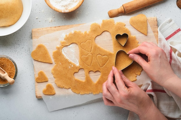 Baking ingredients and kitchen utensils on a white background top view Female or man hands preparing heart sugar cookies Baking sugar cookies Flour eggs sugar spices on kitchen table Flat lay