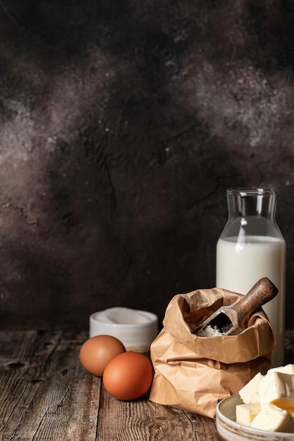 Baking ingredients milk flour butter and eggs on wooden background Dark key rustic style copy space