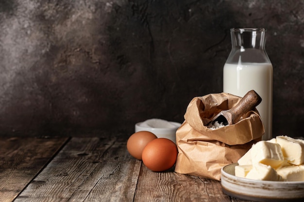 Baking ingredients milk flour butter and eggs on wooden background Dark key rustic style copy space