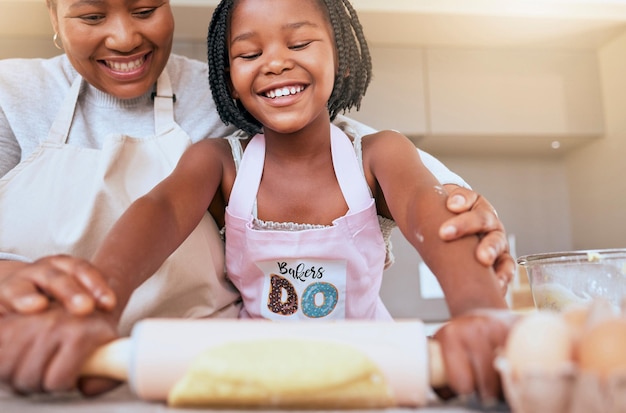 Baking mother and child helping in the kitchen learning and smile for rolling dough together in a house Food happy and African mom teaching a girl kid to bake or cooking in their family home