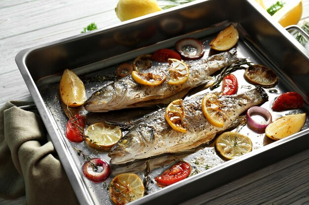 Baking pan with sea bass fish and garnish on wooden background