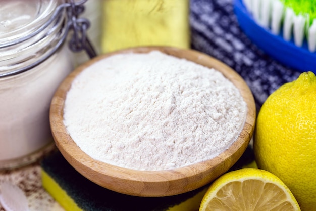 Baking soda with utensils around it, lemon and cleaning products